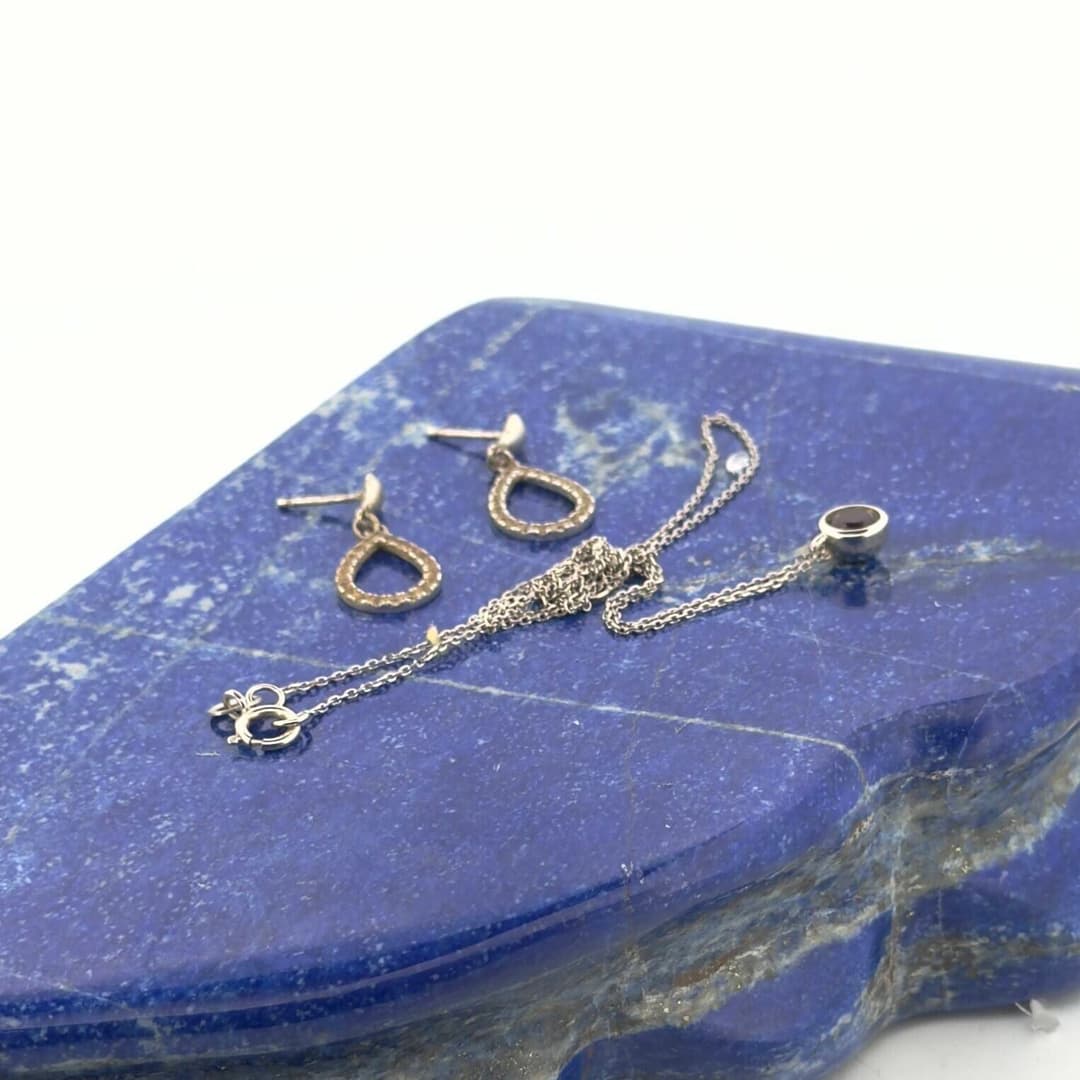 A chain set with a round garnet pendant and a pair of stud e - Lot 212