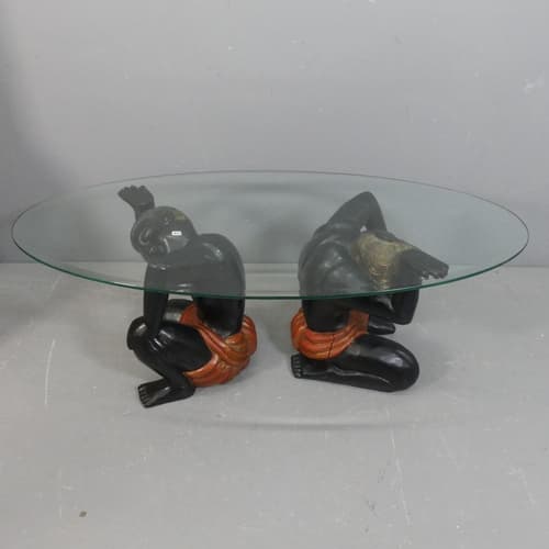 An oval glass-topped coffee table, supported by a pair of pa...